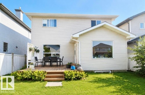 Rear exterior featuring a wood-finish deck with steps to the lawn, a white privacy screen, and white vinyl siding - 3236 27 Avenue Nw, Edmonton, AB - Outdoor With Exterior