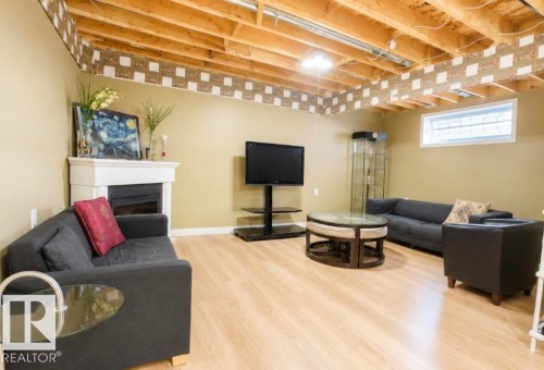 Spacious lower-level room featuring light wood-finish flooring, a white mantel, and an exposed beam ceiling - 3236 27 Avenue Nw, Edmonton, AB - Indoor Photo Showing Basement