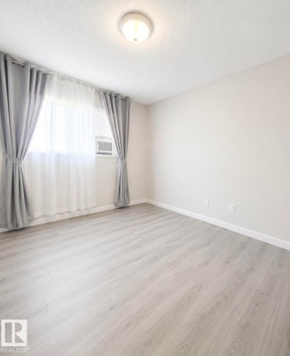 Room featuring light wood-finish flooring, a window with an integrated air conditioning unit, and a flush-mount ceiling light - 3236 27 Avenue Nw, Edmonton, AB - Indoor Photo Showing Other Room