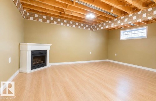 Corner fireplace with white mantel, light wood-finish flooring, and neutral wall paint - 3236 27 Avenue Nw, Edmonton, AB - Indoor Photo Showing Basement