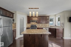 Kitchen featuring dark wood cabinetry, a granite-topped island, stainless steel appliances, a mosaic tile backsplash, and wood-finish flooring - 