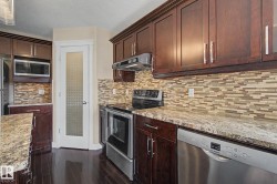 Kitchen featuring dark wood cabinetry, light-toned granite-style countertops, stainless steel appliances, a mosaic tile backsplash, and dark wood-finish flooring - 