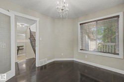 Spacious room featuring dark wood-finish flooring, a crystal chandelier, and a large window with white trim - 