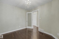 Neutral-toned room featuring a crystal chandelier, dark wood-finish flooring, and white baseboards - 