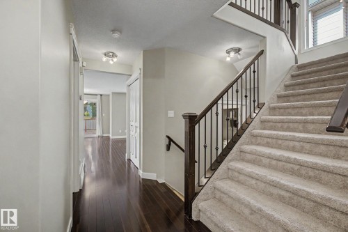 Carpeted staircase with dark wood handrail and black wrought iron balusters - 1047 Leger Boulevard Nw, Edmonton, AB - Indoor Photo Showing Other Room