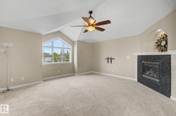 Spacious room featuring vaulted ceilings, a prominent arched window, and a built-in fireplace with a tiled surround - 