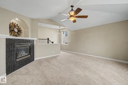 Living area featuring a tiled fireplace with an arched niche, vaulted ceiling, and a ceiling fan with integrated lighting - 