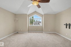 Spacious room featuring vaulted ceilings, a large arched window, a ceiling fan with light fixture, neutral carpeting, and light-colored wall paint - 