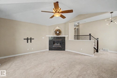 Living area featuring vaulted ceilings, a built-in gas fireplace with dark tile surround, and a ceiling fan - 1047 Leger Boulevard Nw, Edmonton, AB - Indoor With Fireplace