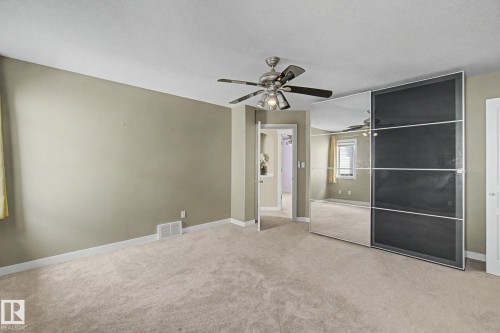 Carpeted room featuring a ceiling fan with integrated lighting, mirrored closet doors, and light neutral wall paint - 1047 Leger Boulevard Nw, Edmonton, AB - Indoor Photo Showing Other Room