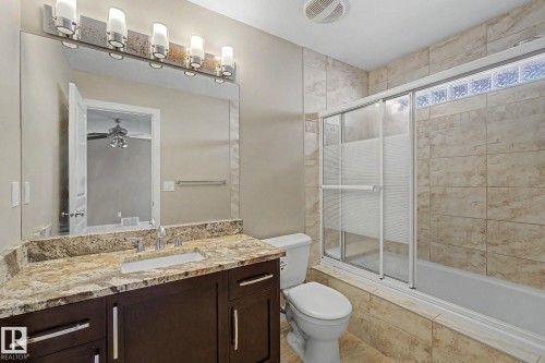 Full bathroom featuring a dark wood vanity with a stone countertop, an integrated sink, and a large mirror - 1047 Leger Boulevard Nw, Edmonton, AB - Indoor Photo Showing Bathroom
