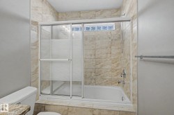 Bathtub and shower combination featuring a glass slider enclosure with frosted panels, light-toned stone tile surround, and a chrome fixture - 
