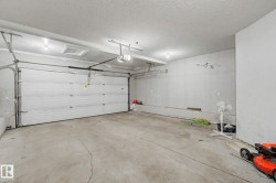Attached garage featuring a white sectional overhead door with an automatic opener, concrete flooring, and ceiling-mounted lighting - 