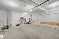 Spacious garage featuring a concrete floor, overhead lighting, garage door opener mechanism, and built-in wall shelving - 