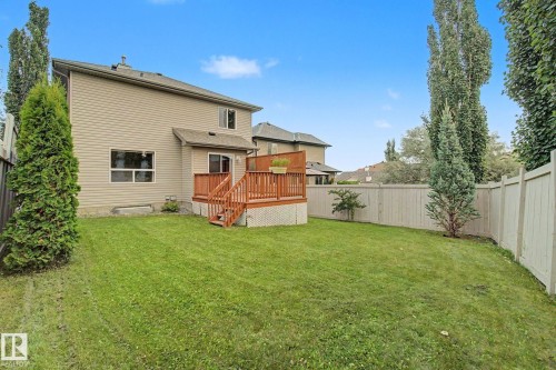 Expansive backyard featuring a wood deck with railings, mature perimeter trees, and full fencing enclosing the property - 1047 Leger Boulevard Nw, Edmonton, AB - Outdoor With Deck Patio Veranda