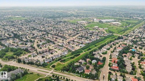 Expansive aerial perspective showcasing a residential development with numerous single-family homes, mature trees, and a tree-lined green space - 1047 Leger Boulevard Nw, Edmonton, AB - Outdoor With View