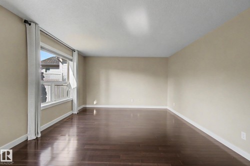 Spacious room featuring rich wood-finish flooring, neutral wall tones, and bright white baseboards - 1047 Leger Boulevard Nw, Edmonton, AB - Indoor Photo Showing Other Room