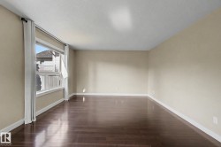 Spacious room featuring rich wood-finish flooring, neutral wall tones, and bright white baseboards - 