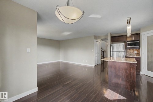 Open concept living area featuring dark wood-finish flooring, a contemporary ceiling light fixture, and a kitchen island with a stone countertop - 1047 Leger Boulevard Nw, Edmonton, AB - Indoor Photo Showing Kitchen