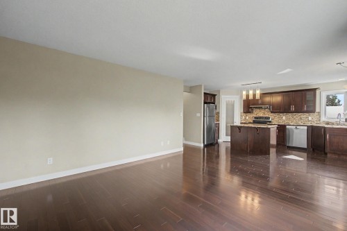 Open-concept living space featuring wood-finish flooring, a kitchen with dark cabinetry, stainless steel appliances, a center island, and pendant lighting - 1047 Leger Boulevard Nw, Edmonton, AB - Indoor Photo Showing Kitchen