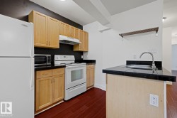 Kitchen featuring wood-finish flooring, natural wood cabinetry, black countertops, white appliances, and a built-in sink on an island - 
