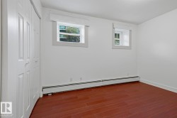 Bedroom featuring rich wood-finish flooring, white walls, and two windows with white trim - 