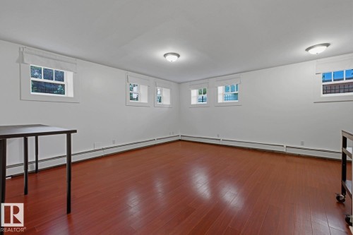 Spacious room featuring rich wood-finish flooring, multiple windows with white trim, white walls, and ceiling-mounted dome light fixtures - #3 9955 114 St Nw, Edmonton, AB - Indoor Photo Showing Other Room