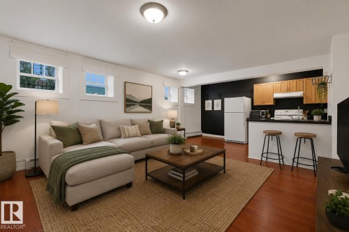 Open-concept living space featuring wood-finish flooring, recessed windows, an integrated kitchen area with wood cabinetry, and a black countertop bar - #3 9955 114 St Nw, Edmonton, AB - Indoor