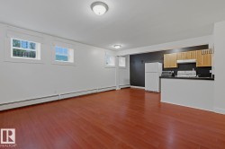 Open-concept living area featuring rich wood-finish flooring, multiple windows with white trim, and a compact kitchen area - 
