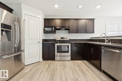 Kitchen featuring dark wood cabinetry, stainless steel appliances, dark countertops, and wood-finish flooring - 
