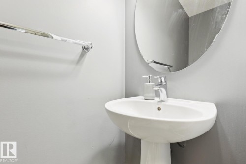 White porcelain pedestal sink with a chrome faucet and an oval wall-mounted mirror - 4058 Morrison Way Nw, Edmonton, AB - Indoor Photo Showing Bathroom