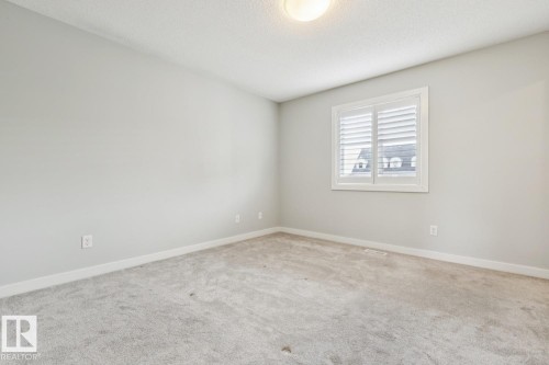 Neutral-toned room featuring a single window with white louvered shutters, light gray wall paint, and a textured carpet flooring - 4058 Morrison Way Nw, Edmonton, AB - Indoor Photo Showing Other Room