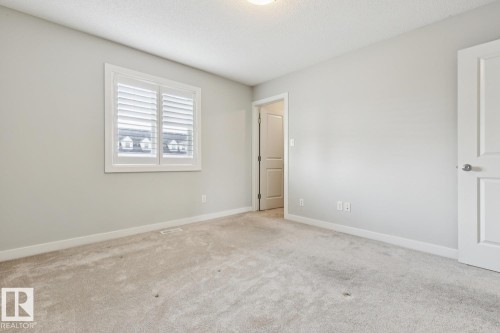 Neutral-toned room featuring a window with white plantation shutters, light-colored carpet, and crisp white trim - 4058 Morrison Way Nw, Edmonton, AB - Indoor Photo Showing Other Room