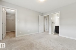 Carpeted room with light gray walls, featuring a walk-in closet with shelving and a bright overhead light - 