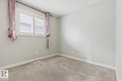 Carpeted room featuring a window with white plantation shutters, light gray walls, and white baseboards - 