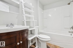 Bathroom featuring a white bathtub with a shower kit, a white toilet, a wood-finish vanity with a white basin, and tile flooring - 