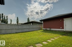 Expansive grassy yard featuring a wood privacy fence, concrete stepping stones, and a red horizontal siding structure with a white exterior door - 