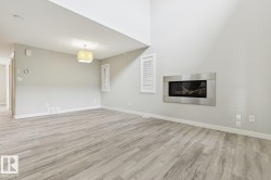 Living area featuring a wall-mounted fireplace with a brushed metal surround, wood-finish flooring, and high ceilings - 