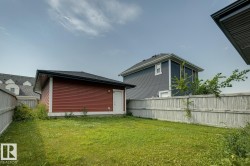 Detached garage featuring red horizontal siding, a black shingle roof, and a white side entry door - 