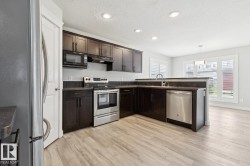 Contemporary kitchen featuring dark wood cabinetry, stainless steel appliances, light wood-finish flooring, recessed lighting, and a breakfast bar - 