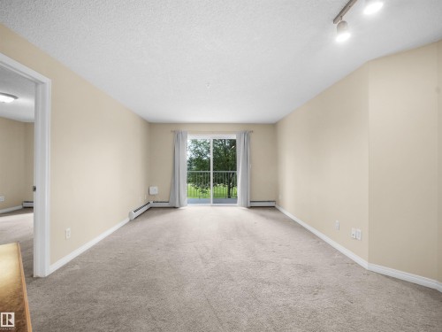 Sliding glass door leading to a balcony with metal railings - #220 245 Edwards Dr Sw, Edmonton, AB - Indoor Photo Showing Other Room