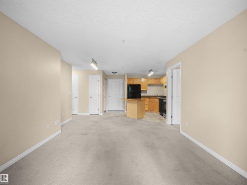 Open-concept living space with light-toned walls and neutral carpeting - #220 245 Edwards Dr Sw, Edmonton, AB - Indoor Photo Showing Other Room