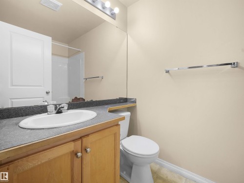 Bathroom featuring a wood-finish vanity with a laminate countertop, an undermount sink, a chrome faucet, and a wall-mounted mirror - #220 245 Edwards Dr Sw, Edmonton, AB - Indoor Photo Showing Bathroom