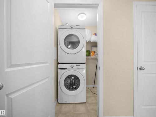 Dedicated laundry area featuring stacked front-load machines - #220 245 Edwards Dr Sw, Edmonton, AB - Indoor Photo Showing Laundry Room