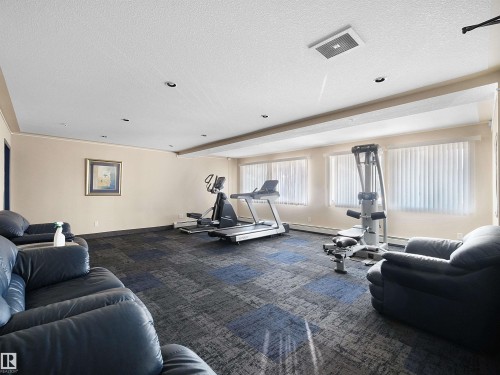 Fitness room featuring patterned carpet flooring, recessed lighting, multiple windows with blinds, and neutral-toned walls - #220 245 Edwards Dr Sw, Edmonton, AB - Indoor Photo Showing Gym Room