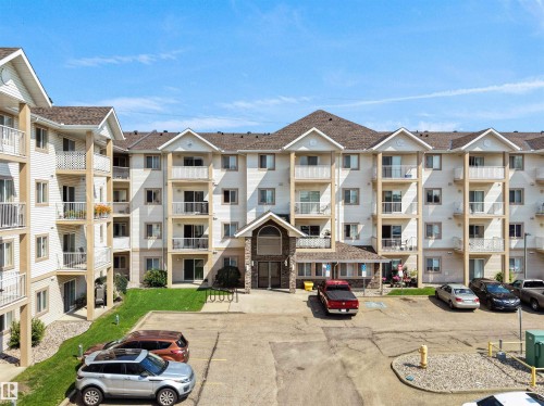 Multi-story residential building featuring balconies, an arched stone entrance, and asphalt parking - #220 245 Edwards Dr Sw, Edmonton, AB - Outdoor With Balcony With Facade