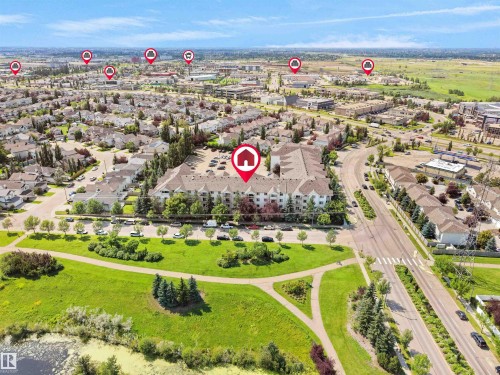 Aerial perspective showcasing a multi-story residential building with surface parking, bordering a green space with walking paths and a body of water - #220 245 Edwards Dr Sw, Edmonton, AB - Outdoor With View