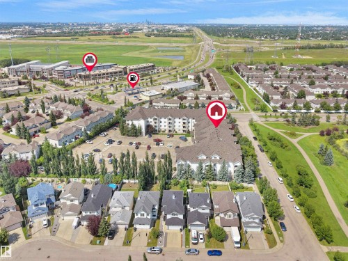 Aerial perspective showcasing residential properties including detached homes and multi-story buildings, alongside a highway and green spaces - #220 245 Edwards Dr Sw, Edmonton, AB - Outdoor With View