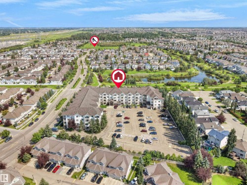 Aerial perspective featuring a multi-story residential building with gabled roofs, surrounded by mature trees and a paved parking area - #220 245 Edwards Dr Sw, Edmonton, AB - Outdoor With View