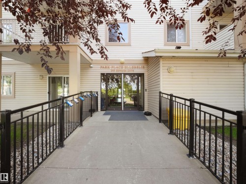 Building entrance featuring a concrete ramp with black metal railings, leading to glass double doors - #220 245 Edwards Dr Sw, Edmonton, AB - Outdoor With Exterior